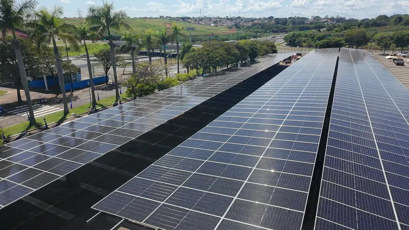 Estacionamento de shopping coberto por fileiras de painéis solares, visto de cima