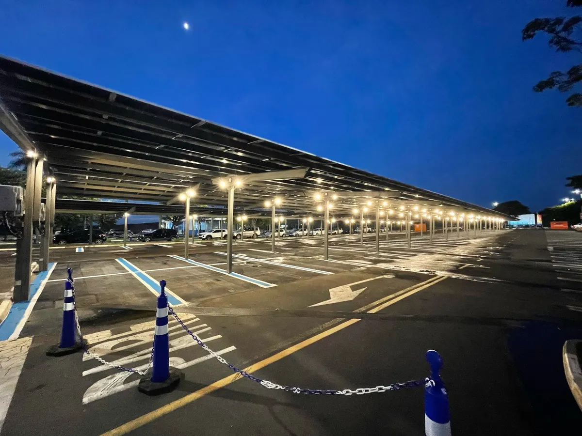 Carport solar sobre as vagas de um estacionamento, ao anoitecer, com luminárias presas sob a cobertura