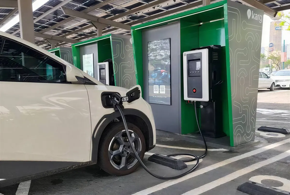 Carro elétrico branco conectado a uma estação de recarga sob o carport solar do shopping