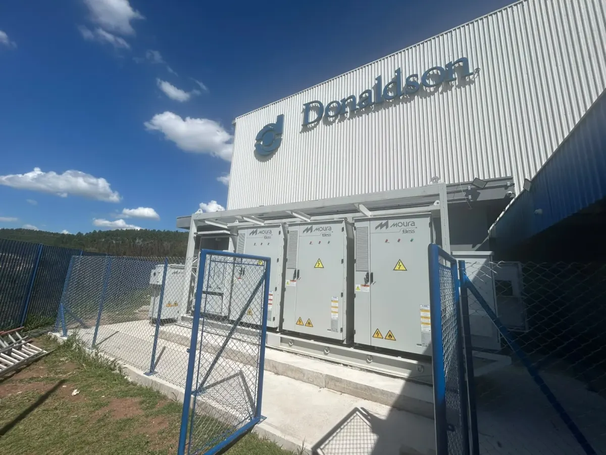Gabinetes do BESS sobre a base de concreto, ao lado do galpão da Donaldson, atrás do alambrado azul