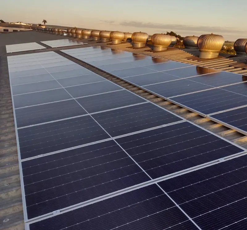 Painéis solares no telhado metálico da Galvisa, com a fileira de exaustores do galpão ao fundo