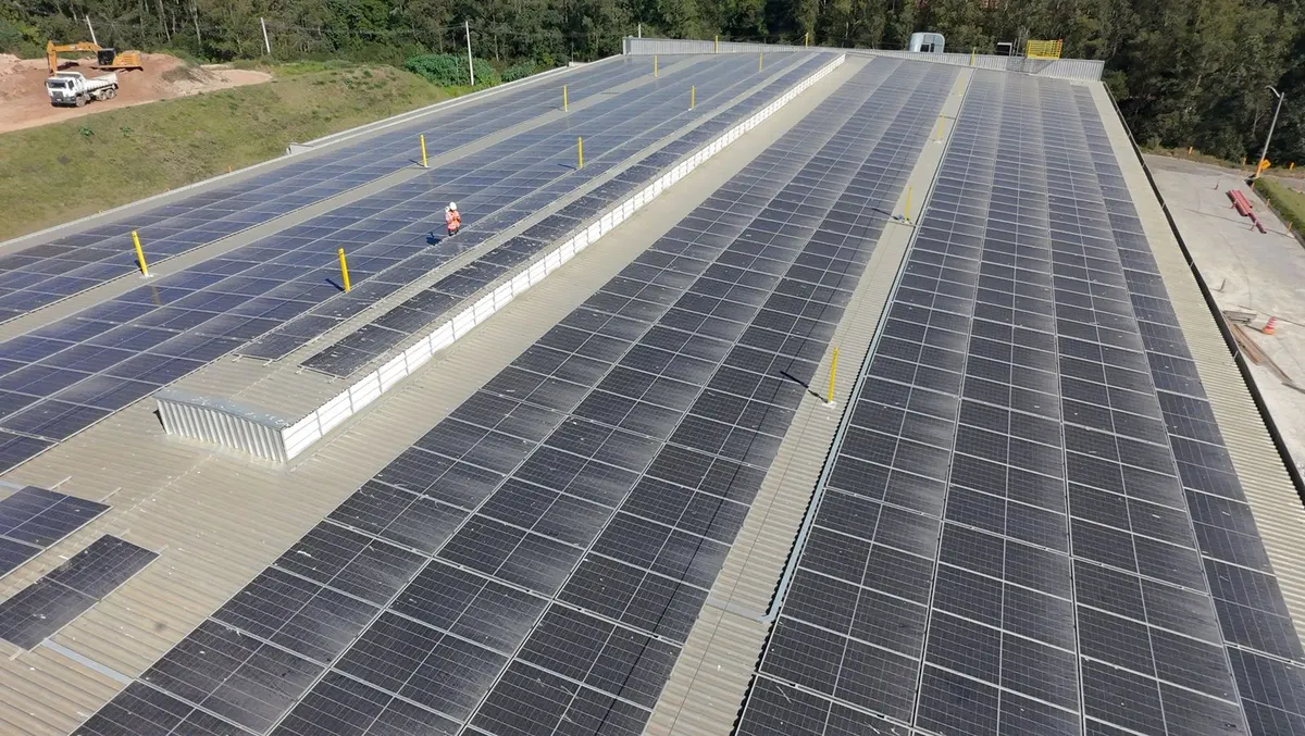 Telhado comprido de galpão industrial coberto de painéis solares, com terreno de terra ao lado