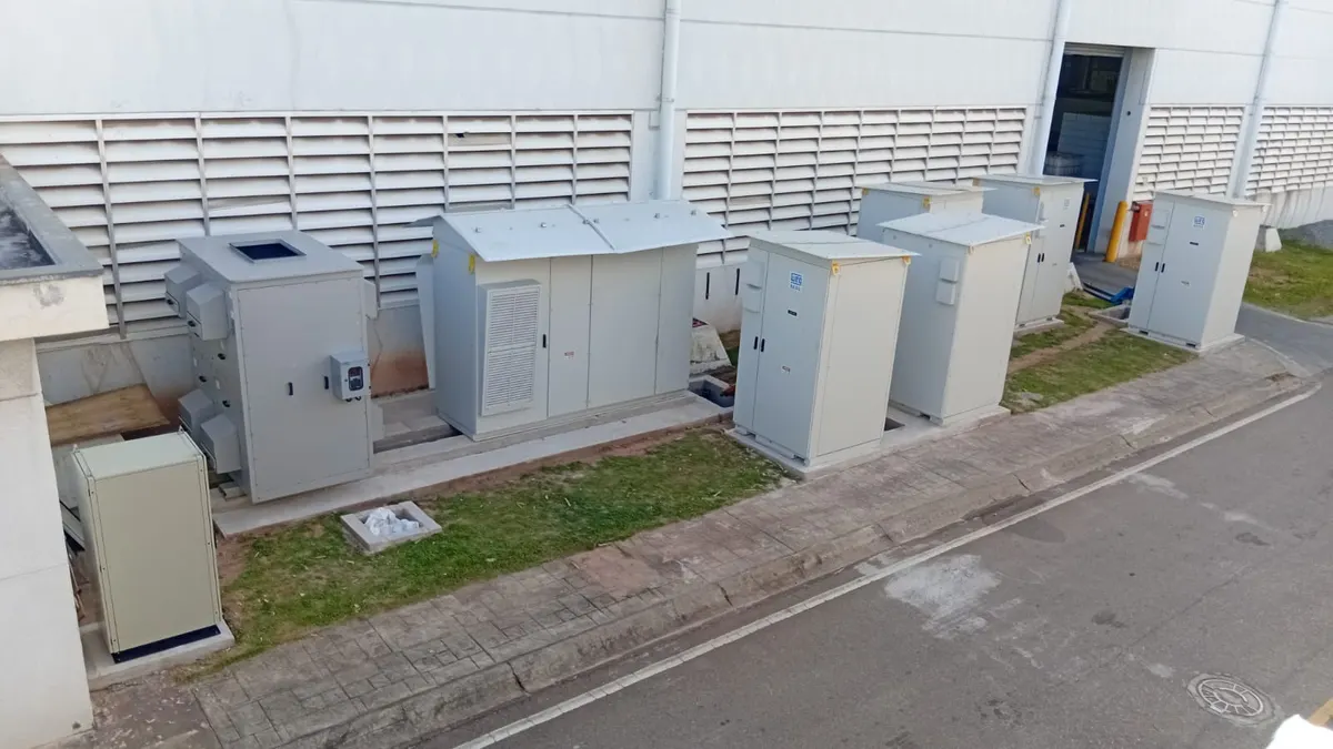Gabinetes de baterias e o transformador de um sistema de armazenamento instalados junto à parede de um galpão industrial