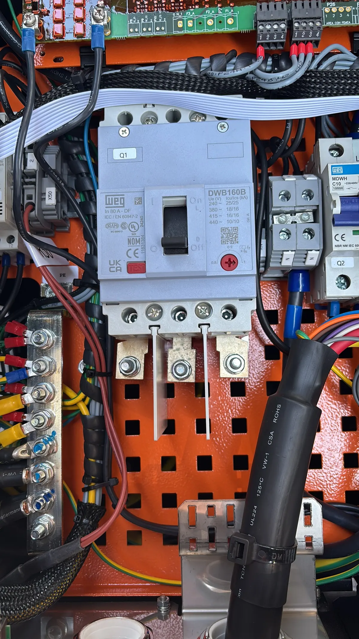 Quadro de proteção de uma estação de recarga aberto, com o disjuntor, os bornes e a chegada dos cabos