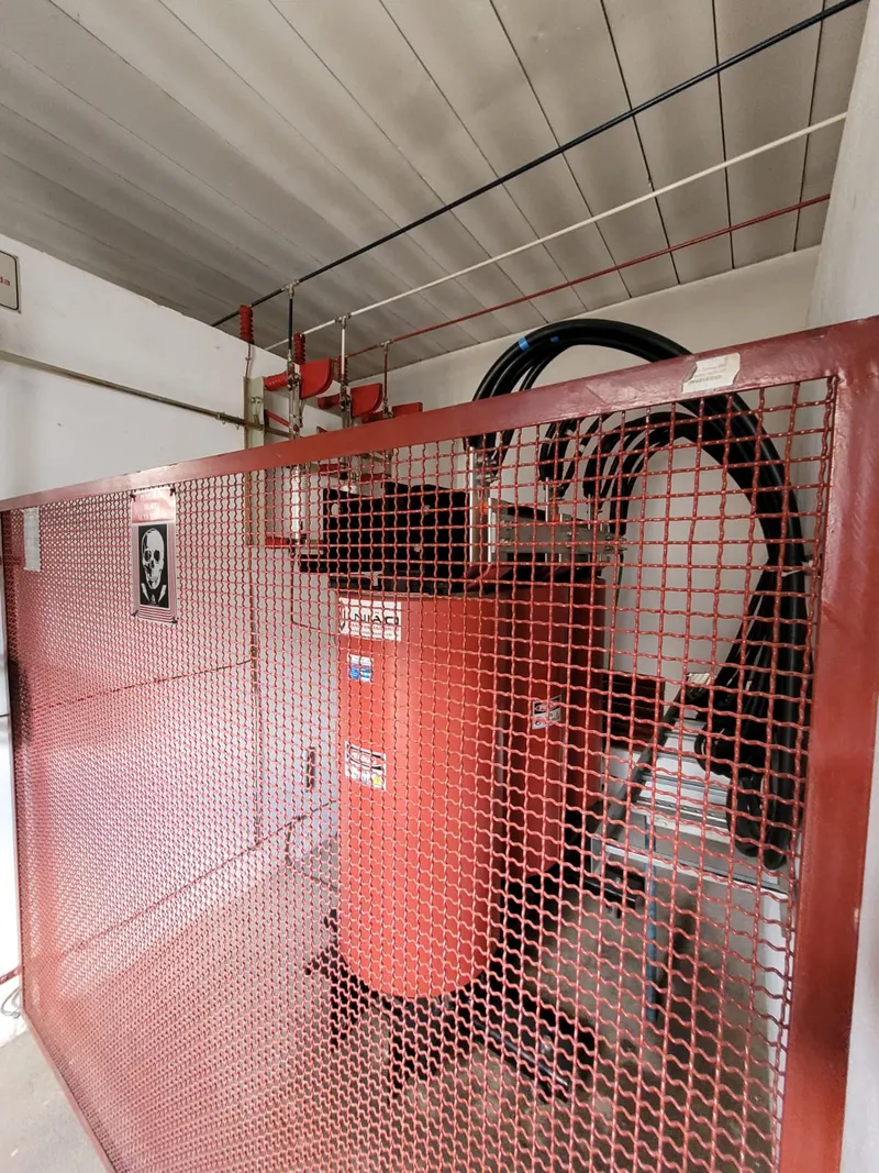 Transformador a óleo dentro da gaiola de proteção de uma cabine, com os cabos de média tensão chegando por cima